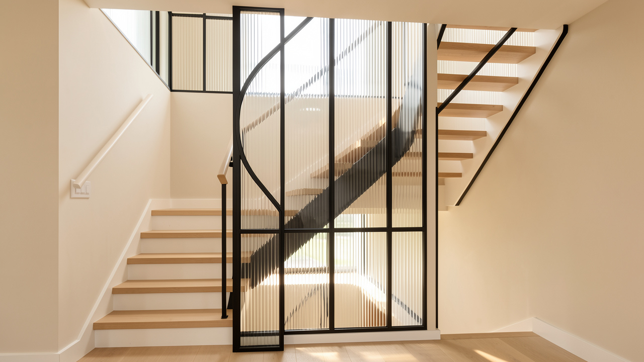 Cage d’escalier contemporaine fermée par des panneaux de verre strié et une structure métallique fine, laissant passer largement la lumière naturelle.
