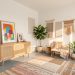Appartement en location aux murs blancs et au sol gris, décoré sans perçage avec des œuvres posées, des tapis, des plantes et des textiles colorés.