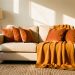 Salon lumineux et chaleureux en automne avec canapé beige, plaid en laine ocre, coussins terracotta, tapis épais et lampadaire en tissu baignés par la lumière de fin de journée.